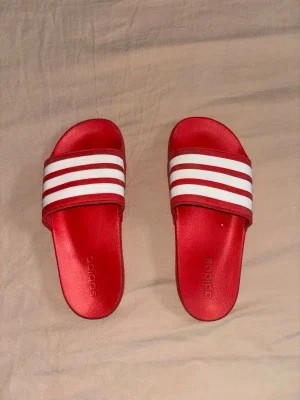 Röda Adidas badtofflor med vita ränder