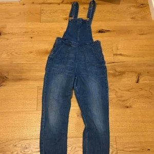 Blå denim hängselbyxor med råa benslut