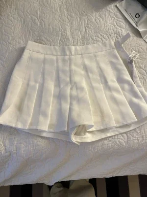Vita plisserade skorts