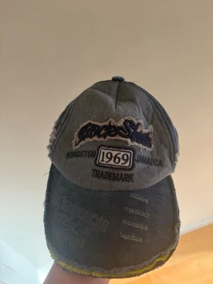 Grå keps med brodyr och slitningar