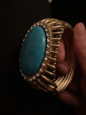 Guldigt armband med blå sten. Det är ett manschettarmband.